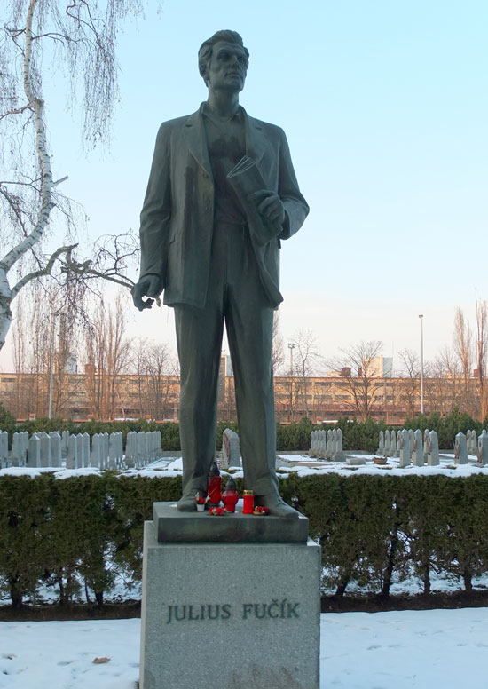 Foto der Julius Fučík Statue (1978) auf den Prager Friedhöfen Olšany von Miloslav Šonka aus dem Jahr 2014. Die Statue stellt Fučík mit einer Zeitung in der Hand dar, während er in die Ferne blickt. Auf den Sockel der Statue sind einige Grabkerzen gestellt.
